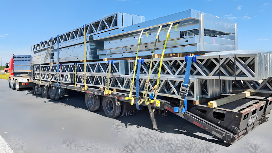 Light gauge steel wall and lattice joist panels securely strapped on a flatbed trailer for modular construction site delivery, produced by light steel framing system.